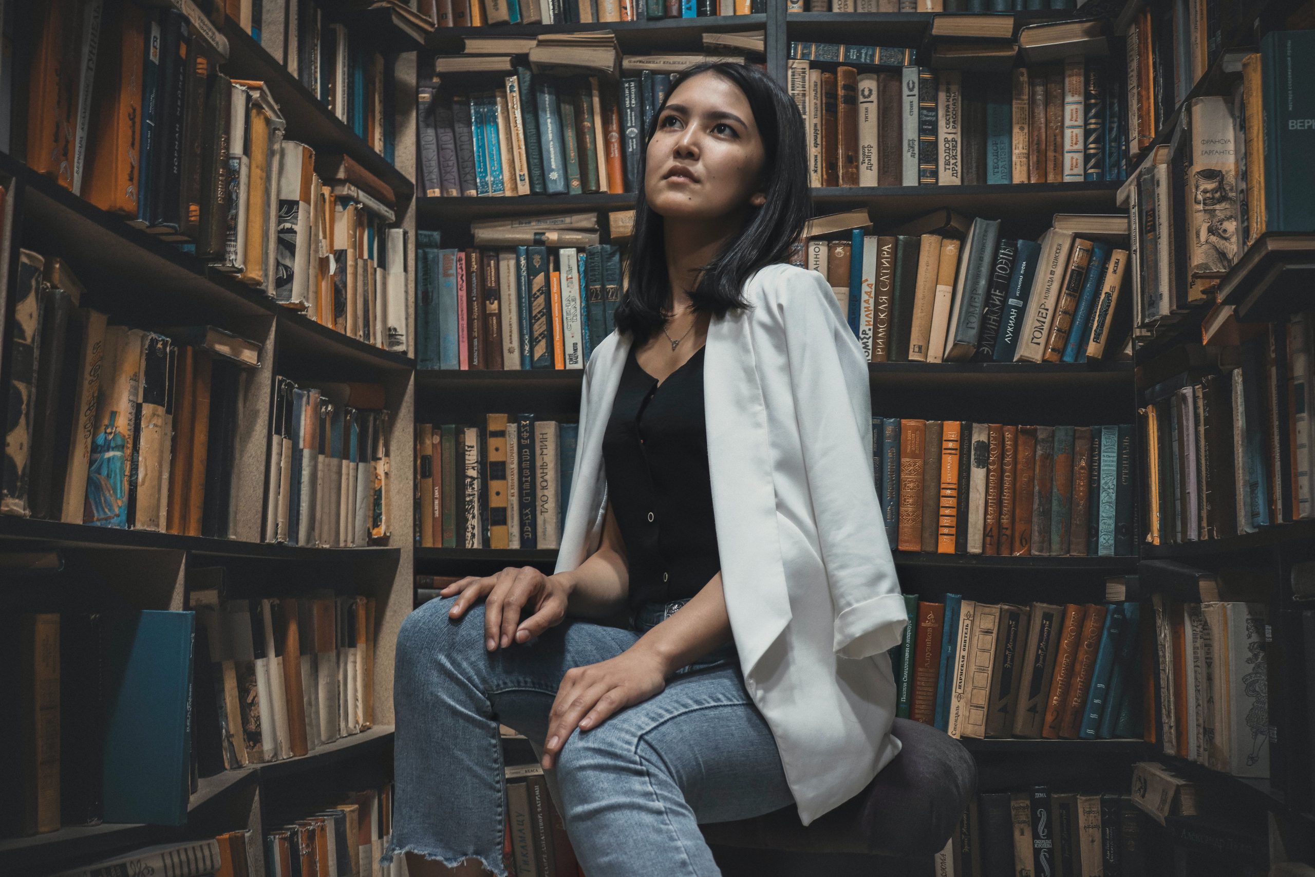 Persona sentada entre estanterías de libros buscando uno que le llame la atención